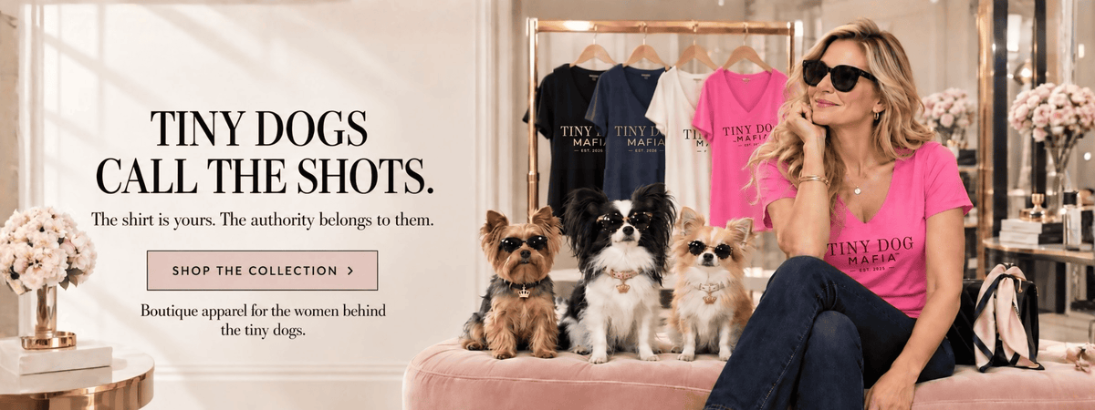 A woman wearing a bright pink T-shirt with 'TINY DOG MAJESTIC' sits on a pink bench with three small dogs in a boutique setting. A text overlay on the left reads 'TINY DOGS CALL THE SHOTS.